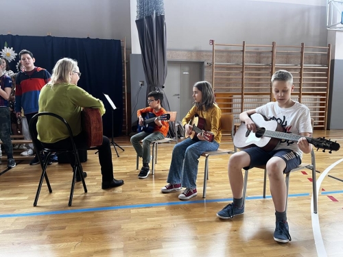 Uczniowie i nauczycielka grają na gitarach. 