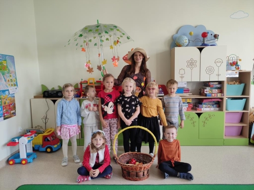 Grupa dzieci wraz z panią pozuje do zdjęcia z koszem z darami jesieni.
